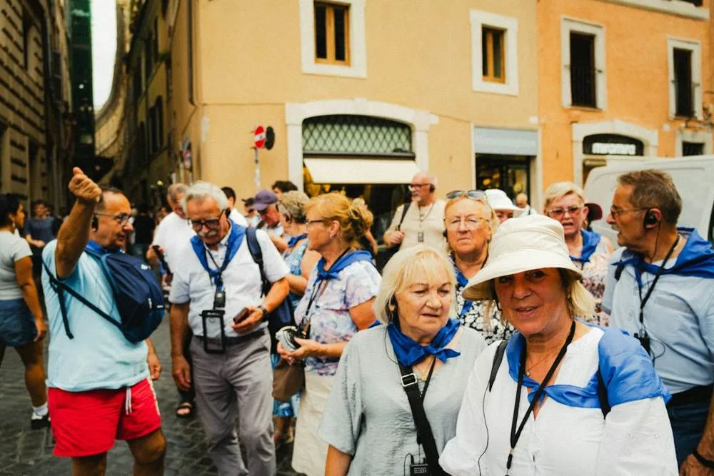A group of older travelers in sun hats and lanyards gathered around a guide on a narrow street